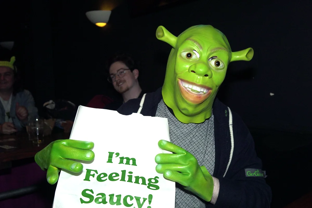 Attendee in a Shrek mask holding a sign